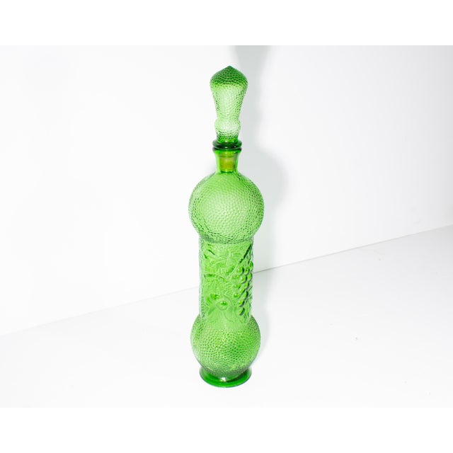 An Empoli green glass bottle that features a raised fruit design. Made in Italy, this light green bottle comes in a...