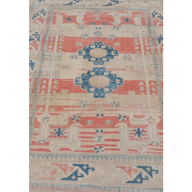 Measures: 4'5 x 6'7 This vintage Oushak has repeating motifs in terracotta, cream, and blue encasing multiple motifs and...