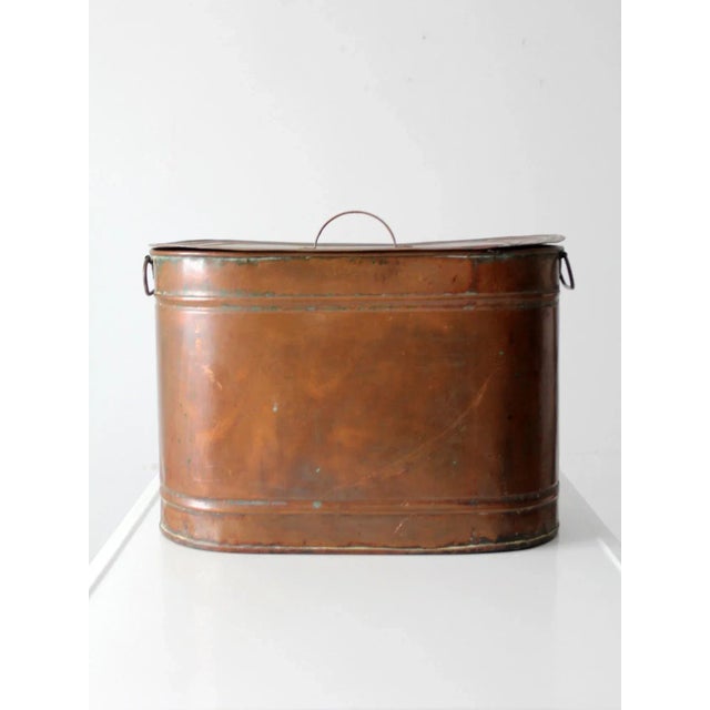 An antique copper boiler featuring a flat lid with copper handle and bail handles on the sides. The warm, aged patina...
