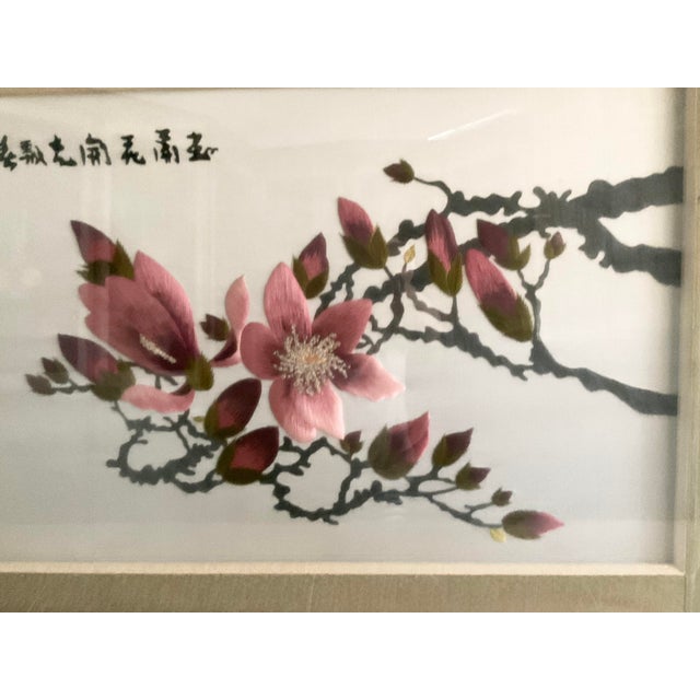 It is embroidered dark pink magnolia in a glass frame. The silk frame in the background has a small light-tone flowers...