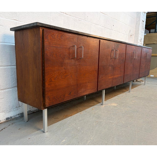 Striking Mid-Century Modern credenza featuring beautifully grained wood veneer, sleek minimalist cabinet doors, and a...