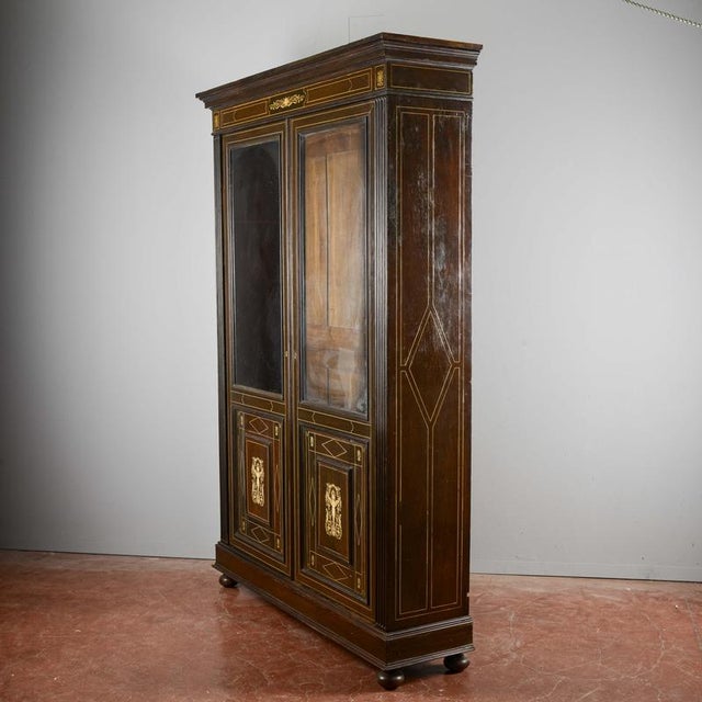 An elegant two-piece display cabinet, a prized antique piece evoking the opulence of the neoclassical or eclectic style,...