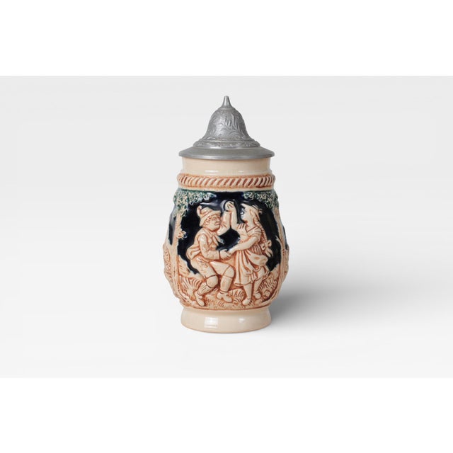 A vintage West German ceramic beer stein in the 1/8-liter size, decorated with molded alpine scenes and finished with a...