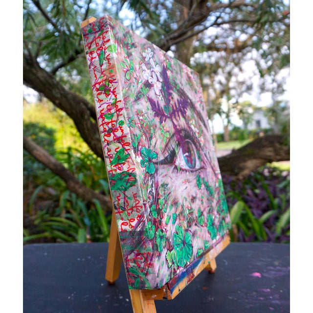 This artwork presents a striking close-up of an eye, intricately intertwined with vibrant foliage and delicate flowers....