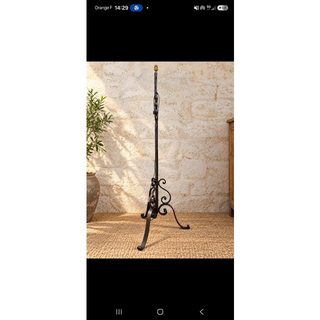 A wrought iron floor lamp dating from the early 20th century. The tripod base rests on three graceful feet ending in...