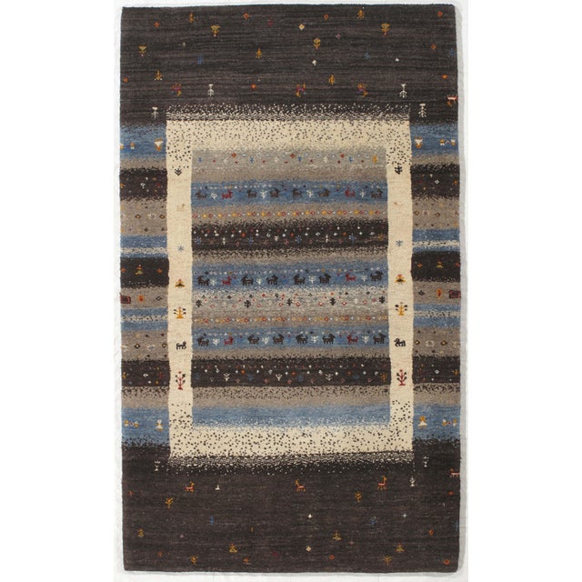 Hand-knotted Indo Gabbeh wool rug featuring horizontal bands in blue, gray, ivory, and charcoal tones with small stylized...