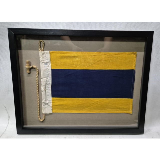 International maritime signal flag of letter 'D', 'DELTA,' set into a shadowbox frame. The cotton flag has a white canvas...