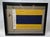 International maritime signal flag of letter 'D', 'DELTA,' set into a shadowbox frame. The cotton flag has a white canvas...