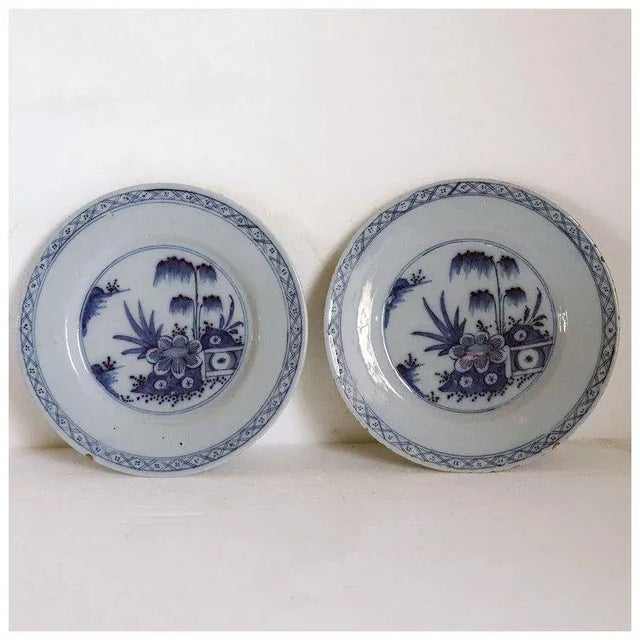 DETAILS A pair of antique Delft faience pottery plates with a Chinese style garden landscape and a diaper pattern border....