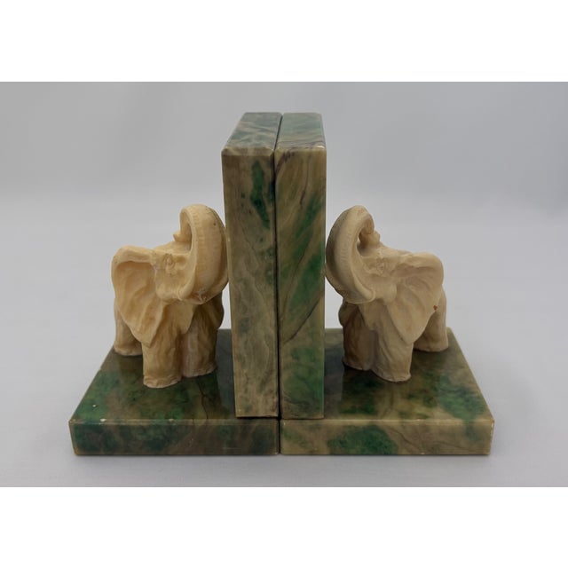 The bookends feature carved cream-colored elephant figures set against substantial green-veined stone uprights and bases....
