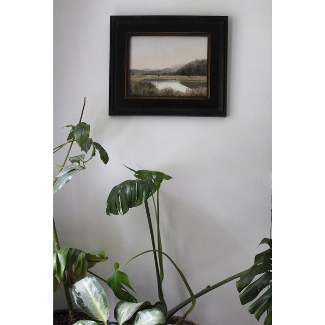 A Kind of Paradise captures a serene landscape where gentle hills meet a tranquil pond, reflecting soft hues of the sky....