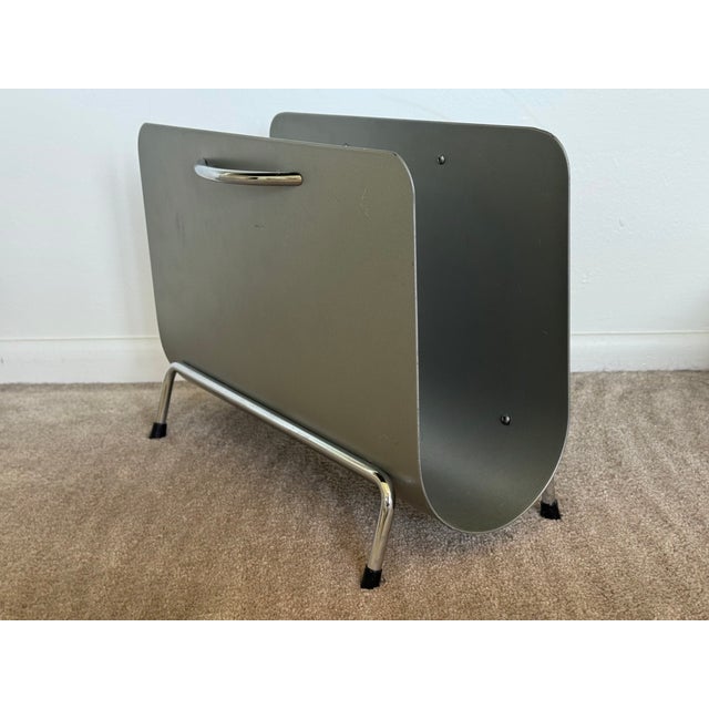 A magazine rack with a curved steel body supported by chromed legs. Accented with chromed handles on each side. The body...