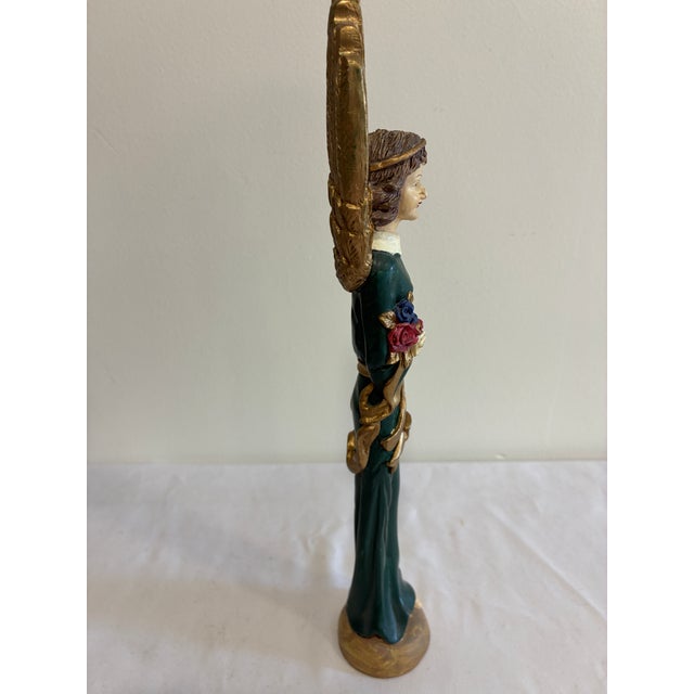 A charming vintage angel figurine featuring dramatic gold feathered wings, a hand-painted face, and flowing green robes...