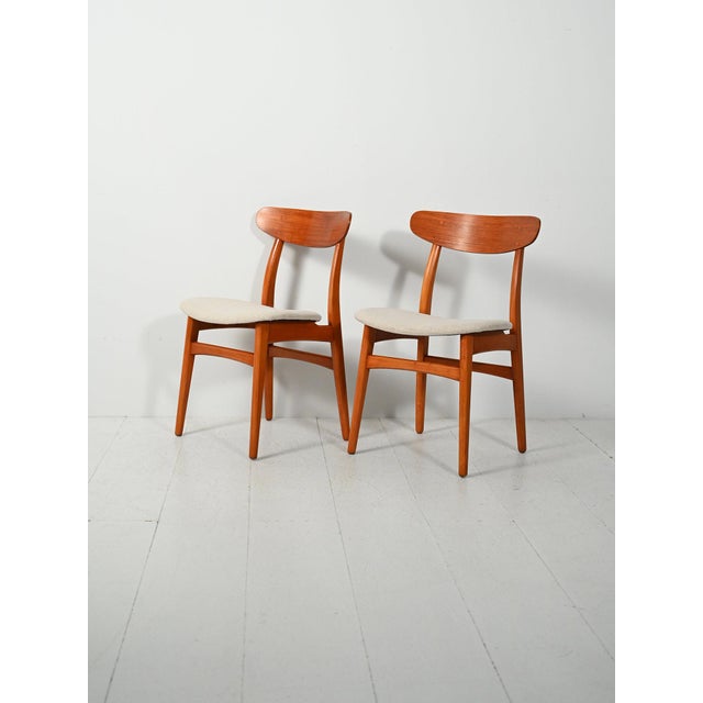 Pair of teak chairs with curved half-moon backrests, reupholstered beige seats, and exposed interlocking details. Pair of...