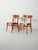 Pair of teak chairs with curved half-moon backrests, reupholstered beige seats, and exposed interlocking details. Pair of...