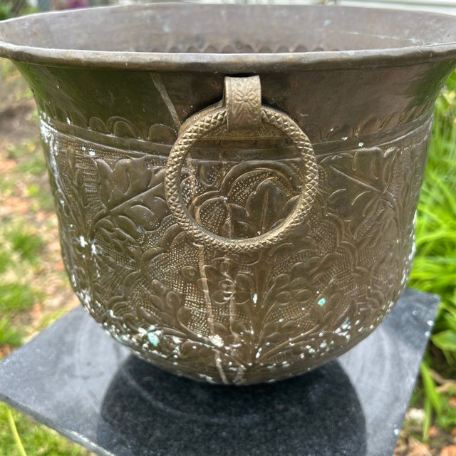 This vintage patinated hammered brass planter/jardiniere with ring handles features intricate repousse floral designs,...