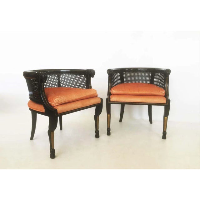 Tailored stately pair of ebonized bergères. These armchairs feature a caned barrel back including a rounded edge over a...