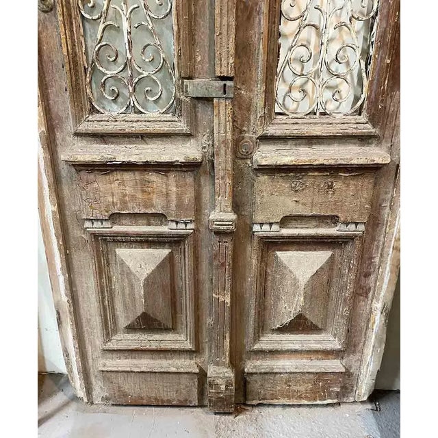 Rustic antique wooden entry doors having wrought iron window grates. Lower section of doors has raised pyramid panels and...
