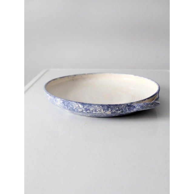 This vintage handmade studio pottery shallow bowl features a cream interior with a blue sponged glaze along the rim and...