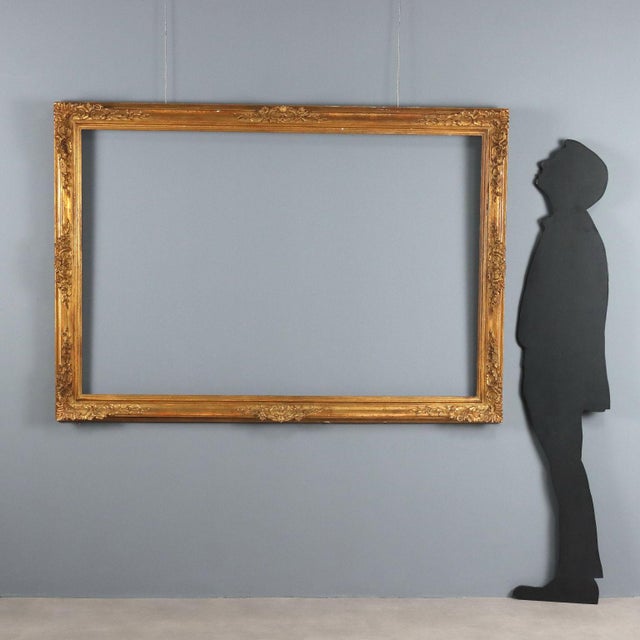 Rectangular gilded wooden frame, embellished with carvings of floral, leaf, and scroll motifs in the corners and in the...