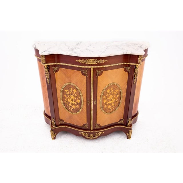 A unique antique chest of drawers featuring a marble top. This piece has a rounded silhouette and is crafted from walnut...