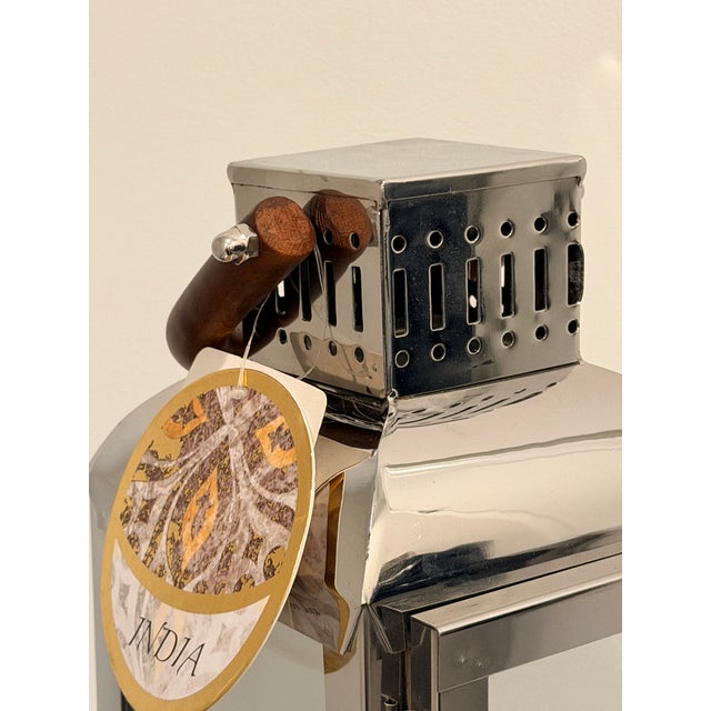 Sleek vintage lantern crafted in polished stainless steel with glass panels and a sculptural wooden handle. Clean,...