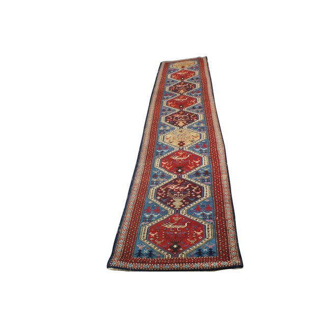 This hand-knotted tribal runner rug features an elongated, vibrant sky-blue field anchored by a continuous chain of...