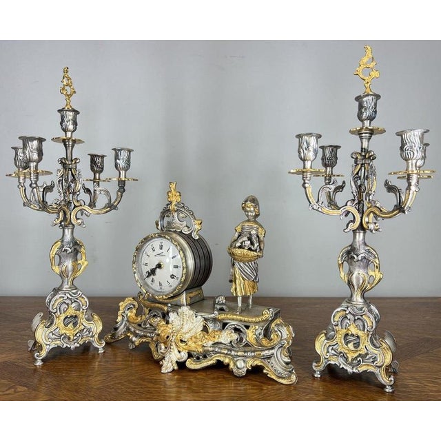 This striking Vintage mantel clock garniture comprises a decorative clock flanked by a matching pair of ornate candelabra,...