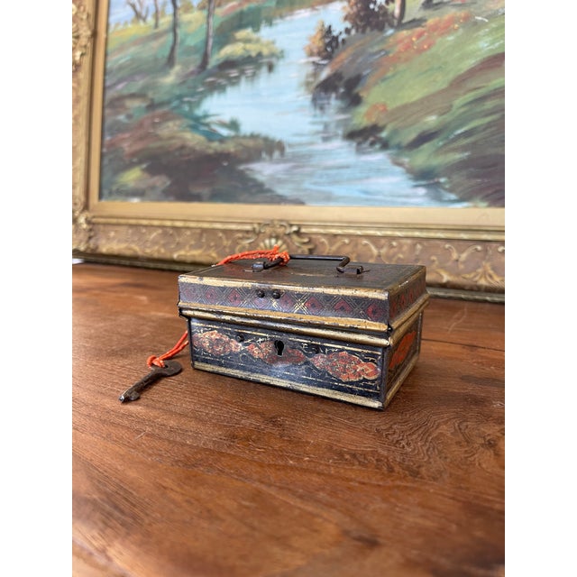This is a 19th-century toleware lock box, crafted from tin and featuring painted decoration in rich tones of red, black,...
