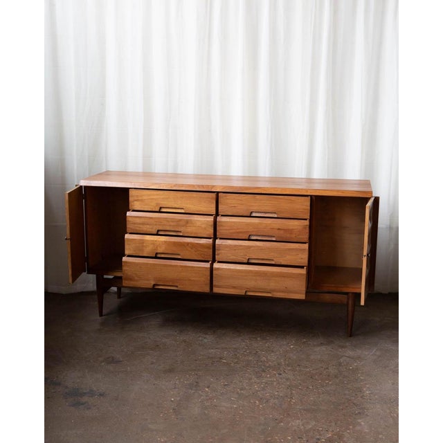 Striking mid-century sideboard crafted in warm butternut, showcasing Bevelacque’s signature geometric detailing. The...