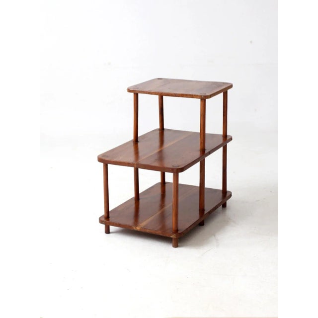 A mid-century tiered side table with a streamlined, architectural silhouette. The three-level design offers graduated...
