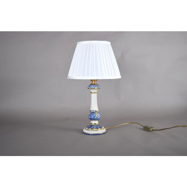 A charming and elegant blue & white ceramic table lamp with refined gilded accents, topped with a crisp pleated white...