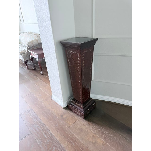 A tall tapered display pedestal in richly carved dark mahogany with intricate relief carving on all four sides. Tiered...