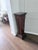 A tall tapered display pedestal in richly carved dark mahogany with intricate relief carving on all four sides. Tiered...