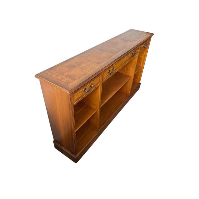 A classic English low bookcase crafted in yew wood, featuring three drawers and open shelving. Clean, traditional design...