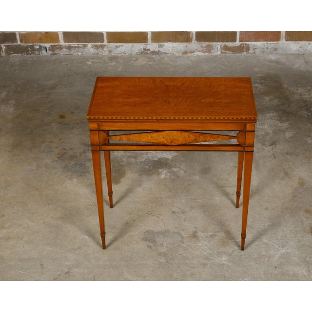 A French folding table from the 19th century with burlwood accents, inlaid rim, elongated diamond motif and tapered legs....