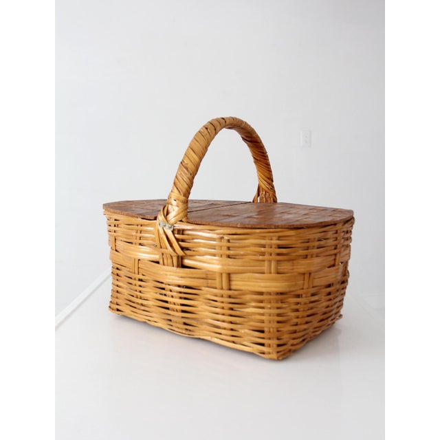 Vintage wicker picnic basket featuring a warm woven finish, divided wood veneer lids, and a wrapped handle. The honey-...
