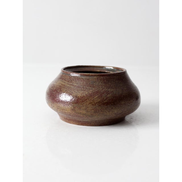 A vintage handmade pottery vessel with a rounded low form and rich brown glaze layered with subtle earthy tonal variation....