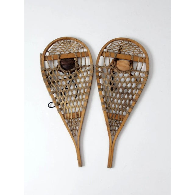 A pair of vintage American wooden trail snowshoes featuring gracefully shaped wood frames, traditional woven webbing, and...