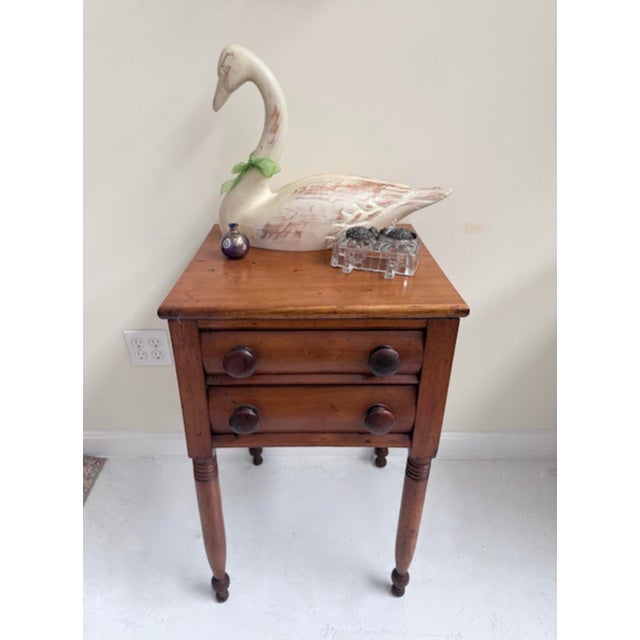 This 19th-century pine two-drawer stand is a beautifully preserved example of early American Federal style craftsmanship....