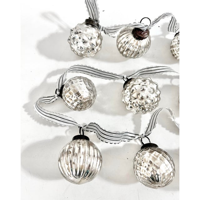 Vintage Christmas ornament garland featuring an assortment of silver mercury-glass ornaments in ribbed, faceted and...