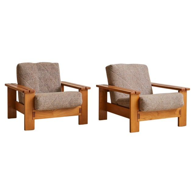 Sold and priced individually. Handcrafted in Paris by Maison Regain around 1970, these oak lounge chairs strike a rare...