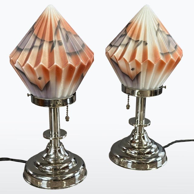 A pair of Art Deco table lamps featuring faceted opaline glass shades in soft orange and purple hues, accented with hand-...