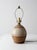 A vintage handmade studio pottery lamp with a rounded ceramic form, carved linear detailing, and layered brown and cream...