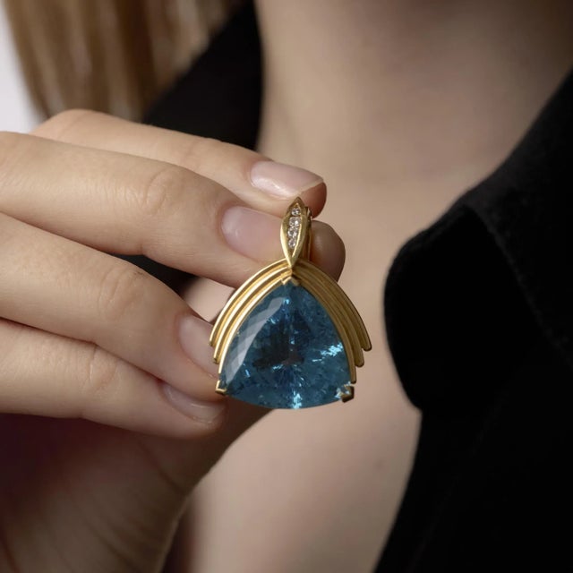 This vintage 18k yellow gold pendant radiates with a stunning 27-carat triangular aquamarine framed by sparkling diamonds,...