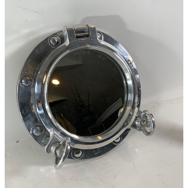 Authentic polished aluminum ship's porthole fitted with a glass mirror. Door is hinged and fitted with two dogbolts. The...