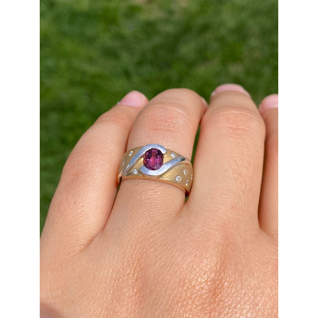 This ring, known as The Aurora, features a captivating oval brilliant cut natural pink tourmaline at its center half bezel...