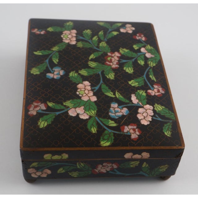 A beautifully crafted vintage Chinese cloisonné enamel box featuring a delicate floral vine motif set against a rich black...