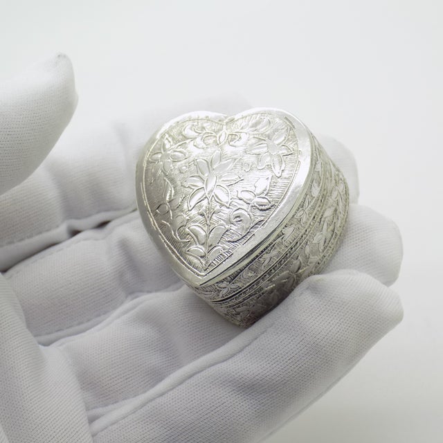 This vintage silver decorative object is shaped as a heart (Cuore) and features a raised floral relief on the lid....