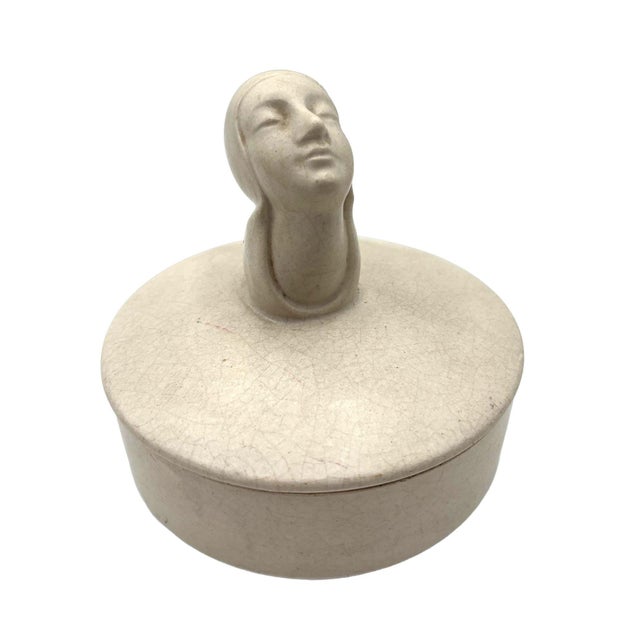 A serene 1930s Art Deco powder box featuring a sculpted woman with her head gently tilted upward and eyes closed,...